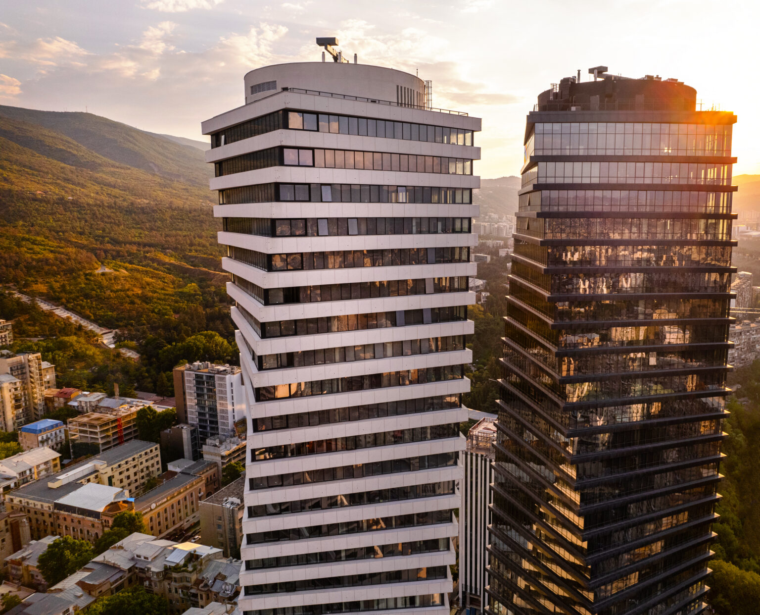 The two twisting Axis Towers at golden hour, with the hills of Vake behind