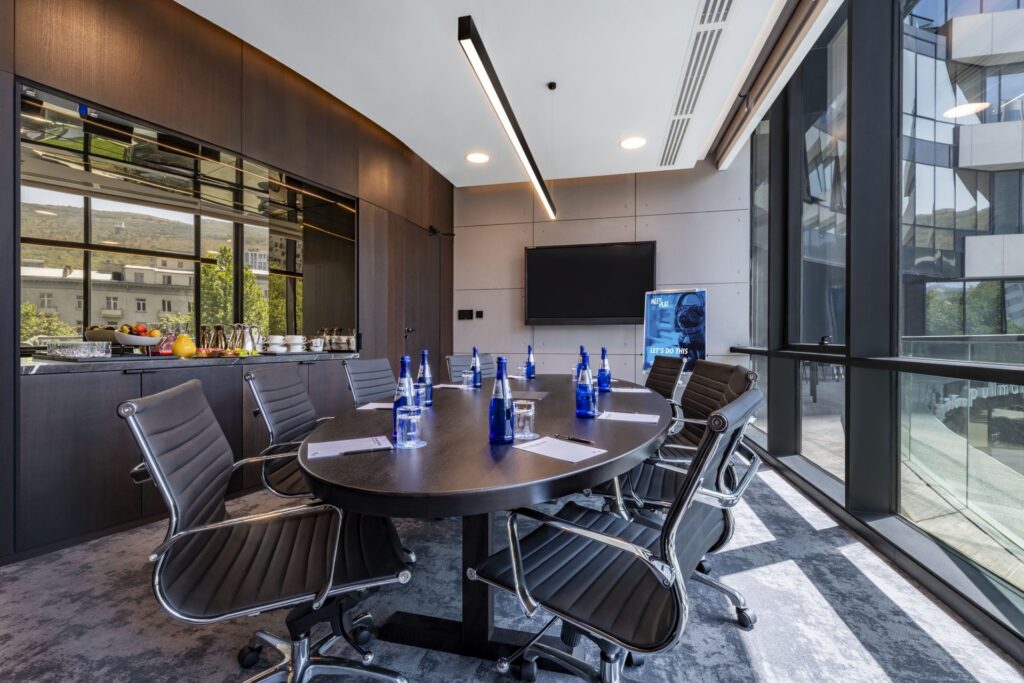 Boardroom with an oval table and a screen, daylight from two sides