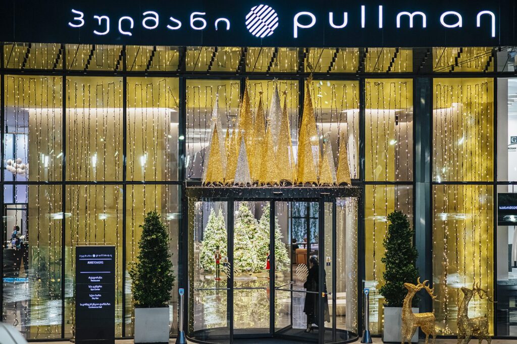 Pullman Tbilisi Axis Towers entrance at night with golden Christmas trees and reindeer