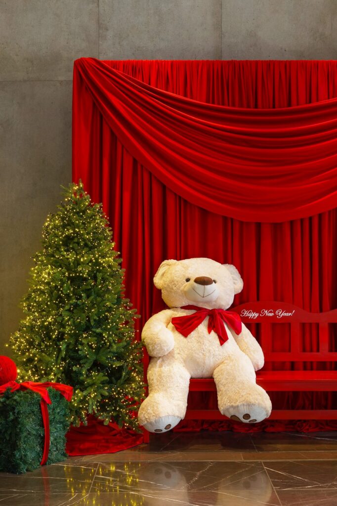 A large white teddy bear between two Christmas trees